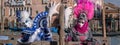 Two women in pink and blue costumes with fans and ornate painted masks in front of the Sagredo Hotel at Venice Carniva