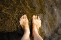 Two women`s bare feet stand on a stone under shallow running water on a summer sunny day. Vacation and travel concept