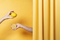 Two women`s hands holding cut and whole lemons on yellow