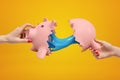 Two women`s hands holding halves of broken piggy bank with blue sticky slime oozing from its insides on amber background