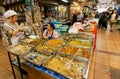 Two women sell asian fast-food with meat inside the market with delicacies and farming products Royalty Free Stock Photo