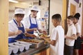 Two women serving food to a boy in a school cafeteria queue Royalty Free Stock Photo