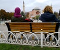 Two women sit in front of the fountain of Sultan ahmet Square and look at the Hagia Sophia