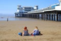 Two women sitting on beach near pleasure pier Royalty Free Stock Photo