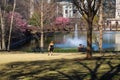 Two women sitting on black metal benches and one woman standing near a green lake in the park surrounded by pink trees Royalty Free Stock Photo