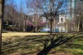 Two women sitting on black metal benches and one woman standing near a green lake in the park surrounded by pink trees Royalty Free Stock Photo