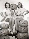 Two women sitting on fence with carved pumpkins