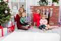 Two women sit together with their young children by the Christmas tree Royalty Free Stock Photo