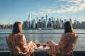 Two women sitting at a table with cups of coffee. View of big modern city