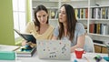 Two women sitting on table studying using laptop reading book at library university Royalty Free Stock Photo