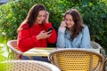 Two women with smartphone  sit in outdoor cafe, sharing the news and  laughing, girls party concept Royalty Free Stock Photo