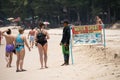 Two women stand beside water sports beach company and talk to a man working at the company. Sunny tropical day at Bang Thao beach