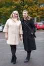 Two women standing together near urban autumn park, full length portrait