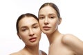 Two women, their flawless skin and delicate features accentuated by subtle makeup, looking at camera with grace against