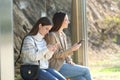 Two women waiting in a bus stop checking phone