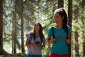 Two women walking along hiking trail path in forest woods during sunny day. Group of friends people summer adventure