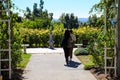 Two women walking along a smooth footpath in the garden surrounded by stone pillars and white wooden awnings