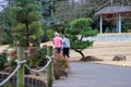 Two women walking in a Japanese garden surrounded by lush green trees and plants with yellow winter grass Royalty Free Stock Photo