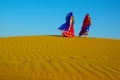 Two women wearing traditional ethnic indian outfits walking on a yellow sand dune Royalty Free Stock Photo