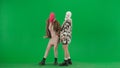 Two women in white and pink balaclavas posing in front of camera as models. Freak women in fur coats on green background