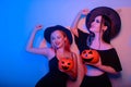 Two women witches hold pumpkins in their hands and dance. Women in neon lights are celebrating a Halloween party. Models smile and