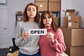 Two women working at small business ecommerce holding open banner puffing cheeks with funny face