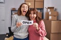 Two women working at small business ecommerce holding open banner smiling and laughing hard out loud because funny crazy joke