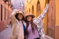 Two women, young and beautiful, with hats and coats, embraced, with one arm up happy and fun. Concept beauty, fashion, autumn,