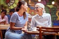 Two women, young and senior, looking each other, smiling, sitting at the table in cafe. family relationship concept Royalty Free Stock Photo