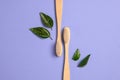 Two wooden bamboo eco friendly toothbrushes and green leaf on purple background. Dental care and zero waste concept.