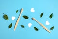 Two wooden bamboo eco friendly toothbrushes, green leaf, white heart on blue background. Dental care, eco friendly.