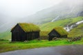 Two wooden barns with grass-covered roofs.