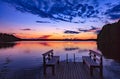 Two wooden bench or chairs on a wood dock facing a lake at sunset in Finland Royalty Free Stock Photo