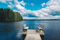 Two wooden chairs bench on a wood pier overlooking a blue lake water with green forest and cloud sky Royalty Free Stock Photo
