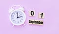 Two wooden cubes and a block with the text SEPTEMBER 01 and a white alarm clock on a light pink background. Back to school concept Royalty Free Stock Photo