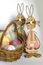 Two wooden Easter bunnies near a wicker basket with three crocheted eggs in front of a bright background Royalty Free Stock Photo