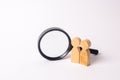 Two wooden human figure stands near a magnifying glass on a white background. The concept of the search for people and workers.