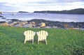 Two wooden lawn chairs set near the shore with a view of the harbor in the lobster village of Tenants Harbor, ME