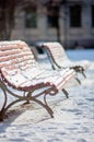 Two wooden park benches covered in snow in the park on a cold and sunny winter day. Wooden and metallic snow-covered benches with Royalty Free Stock Photo