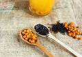 Two wooden spoons with vitaminic healthy sea buckthorn berries and black tea over sackcloth background. cooking, Royalty Free Stock Photo