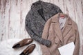 Two woolen coat, brown patent leather shoes on a white fur, white blank sheet, a wooden background. Fashion concept.
