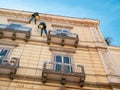 Two workers cleaning facade of historical house hanging on ropes