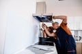 Two workers, handyman in uniform installing or repairing a kitchen extractor, replacing filter in cooker hood Royalty Free Stock Photo