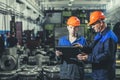 Two workers at an industrial plant with a tablet in hand, working together manufacturing activities