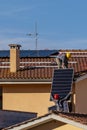 Two workers pass solar panels to each other to be mounted on top of a red tiled roof to install a photovoltaic system Royalty Free Stock Photo