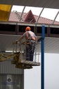 Two workers repair the roof near the railway station. One worker is in a lift with a cradle, the second is on the roof