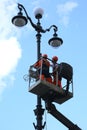 Two workers repair a three-lamp electric lantern