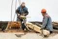 Two workers are repairing the roof of an old building. The carpenter holds a chainsaw in his hand. A wooden beam is attached to Royalty Free Stock Photo