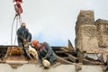 Two workers are repairing the roof of an old building. The carpenter holds a chainsaw in his hand. A wooden beam is attached to Royalty Free Stock Photo