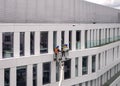 Two workers wearing safety harness wash office building facade at height standing in a crane cradle or aerial platform Royalty Free Stock Photo